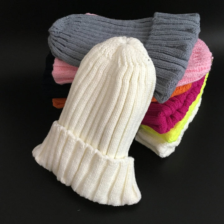 Weiße Strickmütze aus Wolle, gestapelt auf bunte Mützen, Wintermode Accessoire.