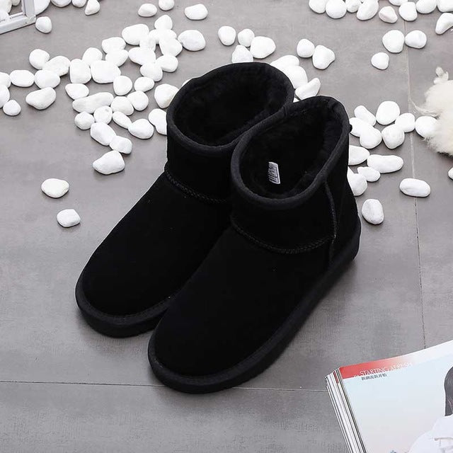 Schwarze Winterstiefel aus Wildleder mit Fellfutter auf grauem Boden, umgeben von weißen Steinen.