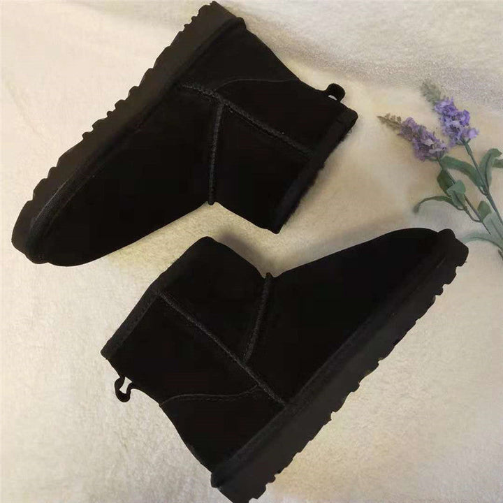 Schwarze Winterstiefel aus Wildleder, flach, mit rutschfester Sohle, auf beigem Hintergrund.