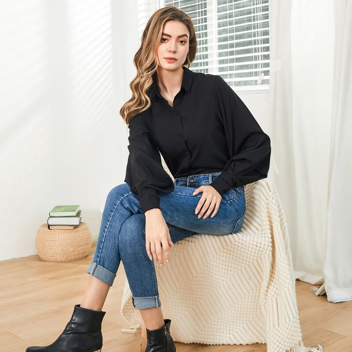 Frau in schwarzer Bluse und blauen Jeans sitzt auf Stuhl, modische Kleidung, Innenraum.