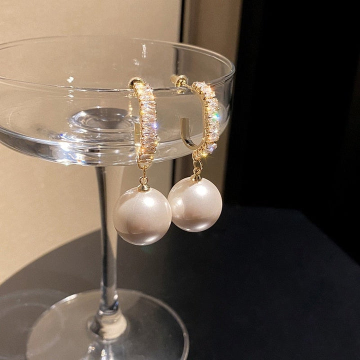 Goldene Ohrringe mit Perlenanhänger, funkelnde Kristalle, eleganter Schmuck, luxuriöses Design.