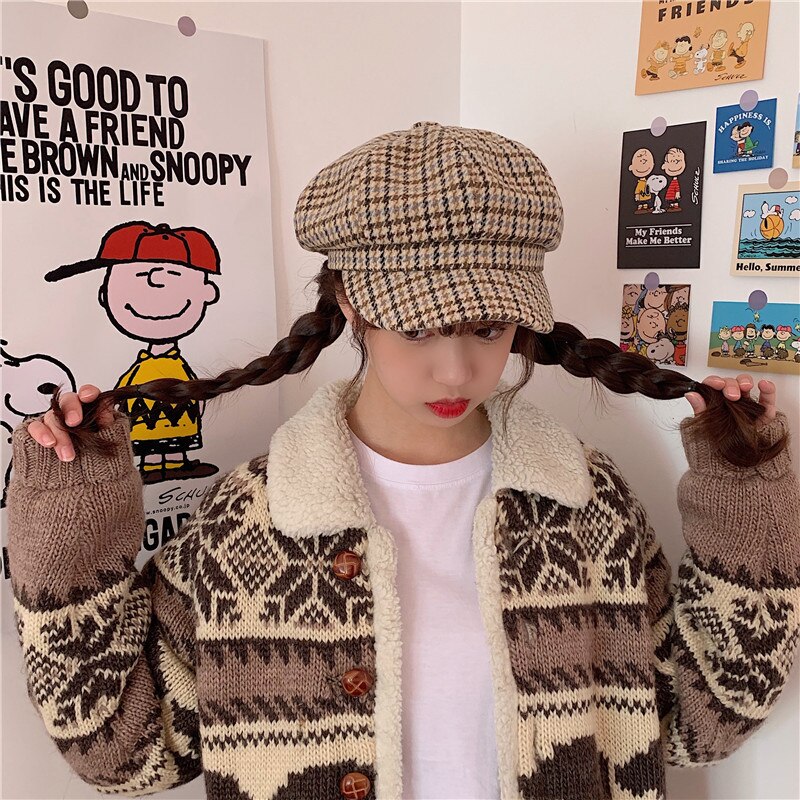 Frau mit Zopfmütze, kariertem Hut, Strickjacke, Peanuts-Poster im Hintergrund.
