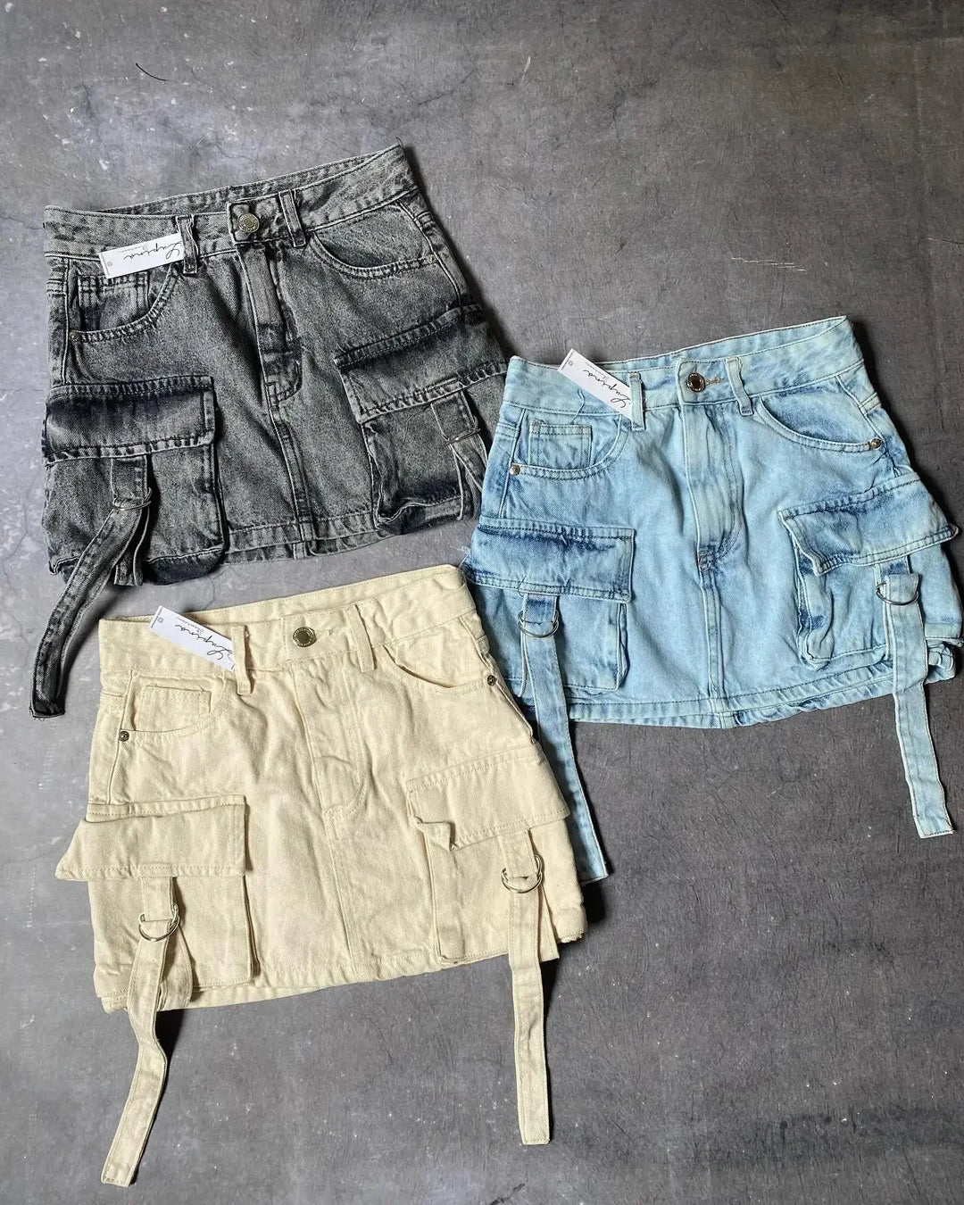 Drei Damen-Jeansröcke, A-Linie, mit Taschen, in Schwarz, Blau und Beige auf grauem Hintergrund.