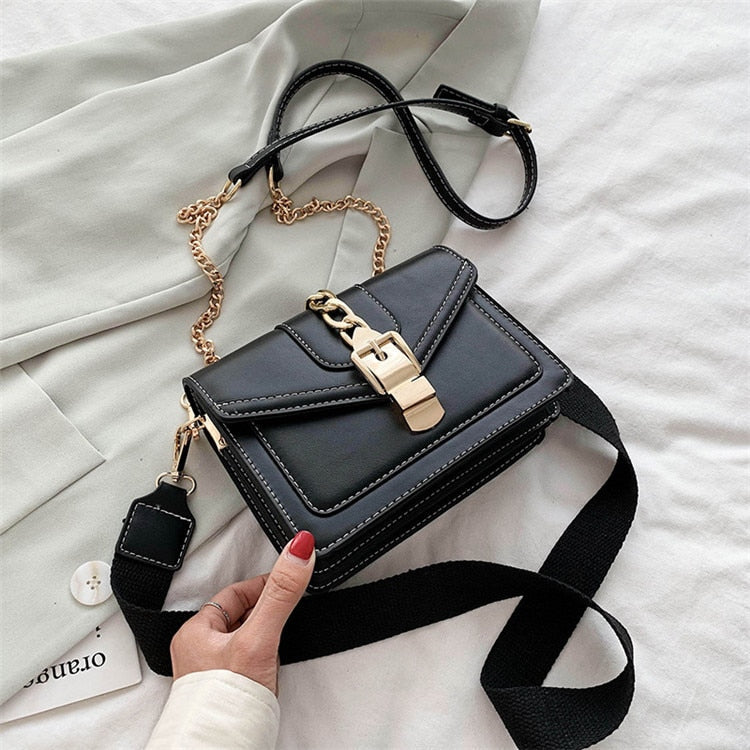 Schwarze Lederhandtasche mit goldener Kette und Schnalle auf weißem Hintergrund.