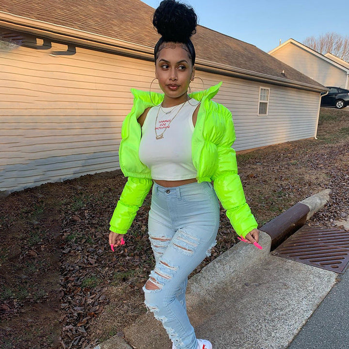 Frau in neongrüner Daunenjacke, weißem Top und zerrissenen Jeans im Freien.