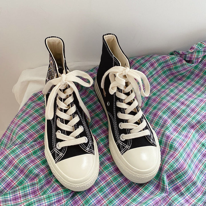Schwarze High-Top-Sneaker mit weißen Schnürsenkeln auf kariertem Stoff.