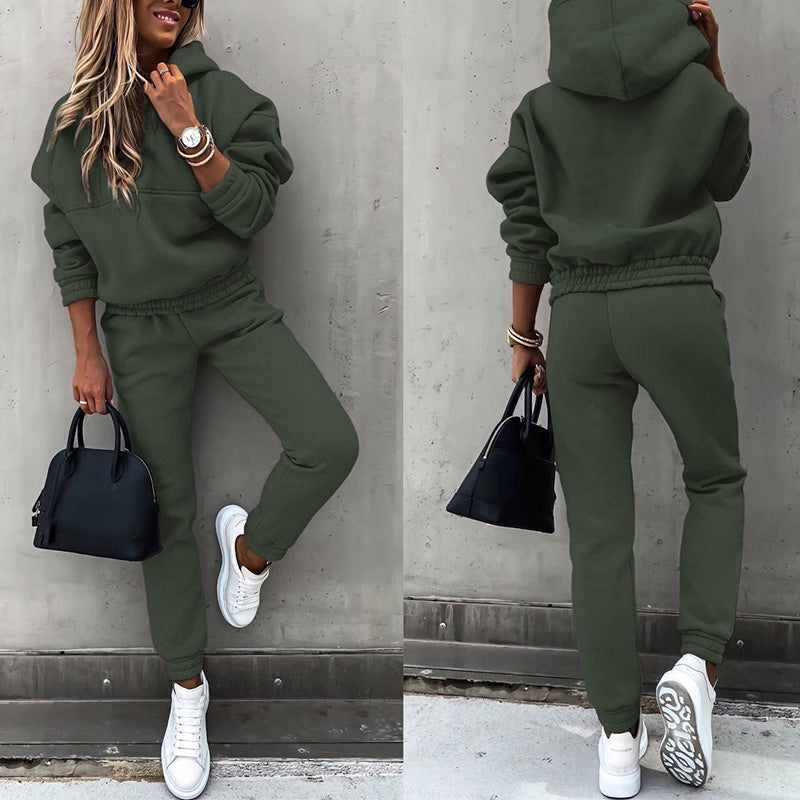 Frau in olivgrünem Jogginganzug, Kapuzenpullover, weiße Sneaker, schwarze Handtasche.