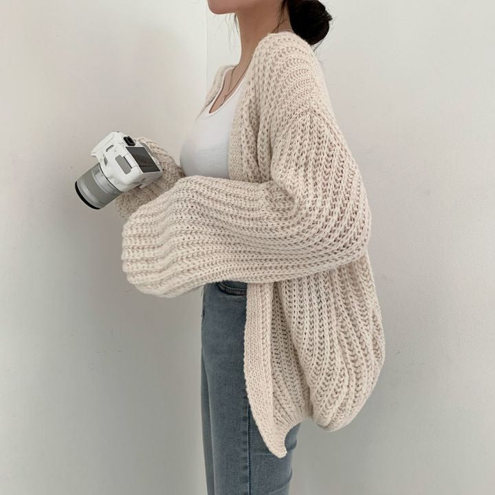 Frau mit cremefarbenem Strickcardigan, Kamera in der Hand, lässiger Look, Modefotografie.