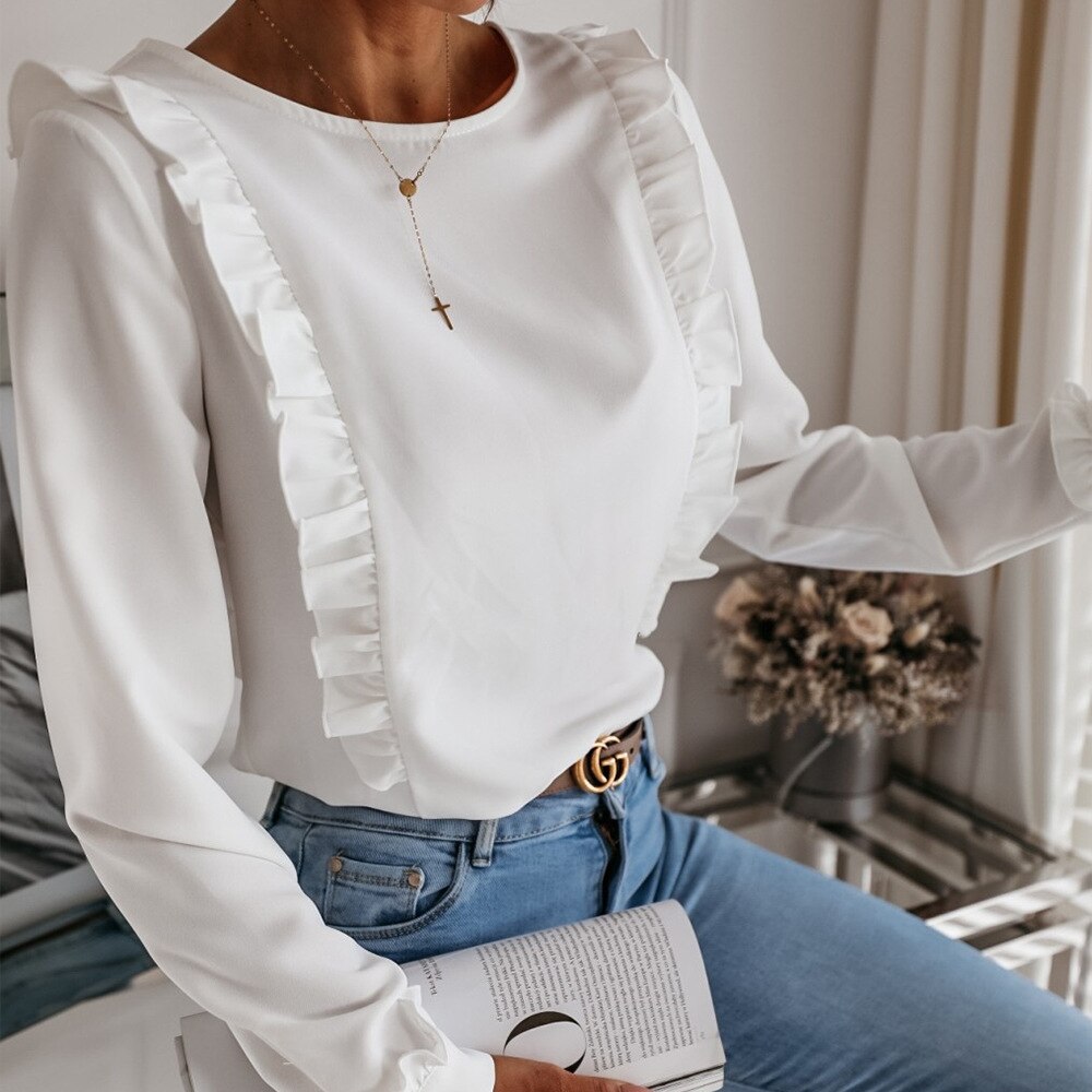 Frau in weißer Rüschenbluse, blaue Jeans, goldene Halskette, modisch, elegant, Innenraum.