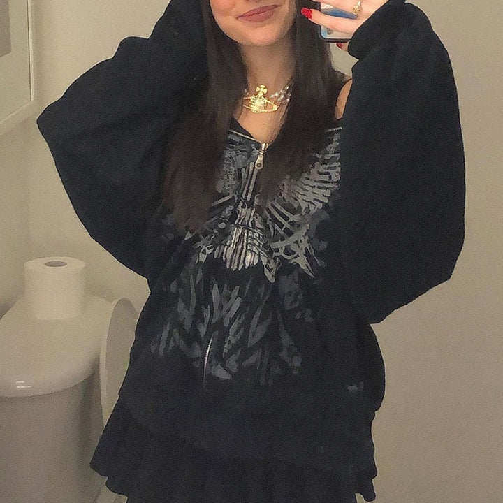 Frau in schwarzem Kapuzenpullover mit Totenkopf-Design, schwarzer Rock, modisches Outfit.