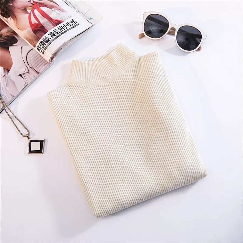 Beigefarbener Rollkragenpullover aus Strick, gefaltet, neben Sonnenbrille und Zeitschrift.