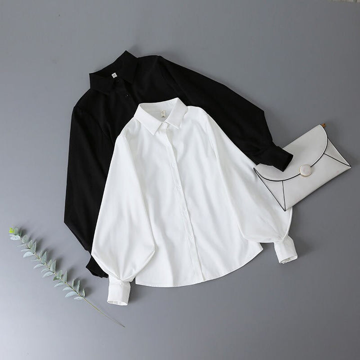Schwarze und weiße Bluse aus Baumwolle mit Umschlagtasche auf grauem Hintergrund.