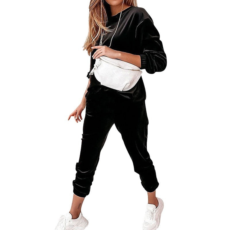 Frau in schwarzem Jogginganzug mit weißer Gürteltasche und weißen Sneakers.
