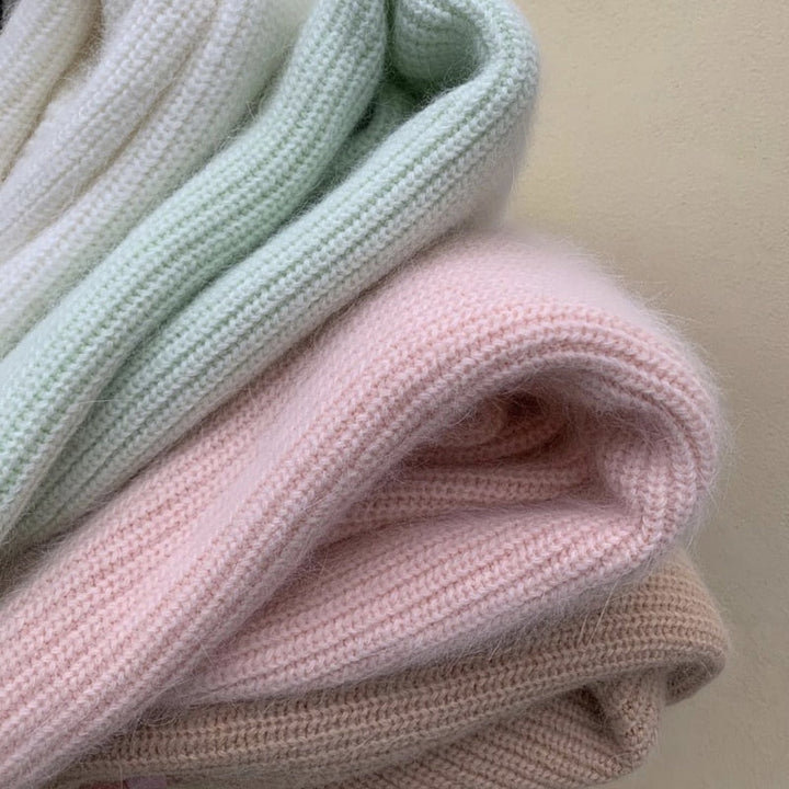 Weiche Strickdecken in Pastellfarben, rosa, grün, beige, aus Wolle, gemütlich, warm, dekorativ.