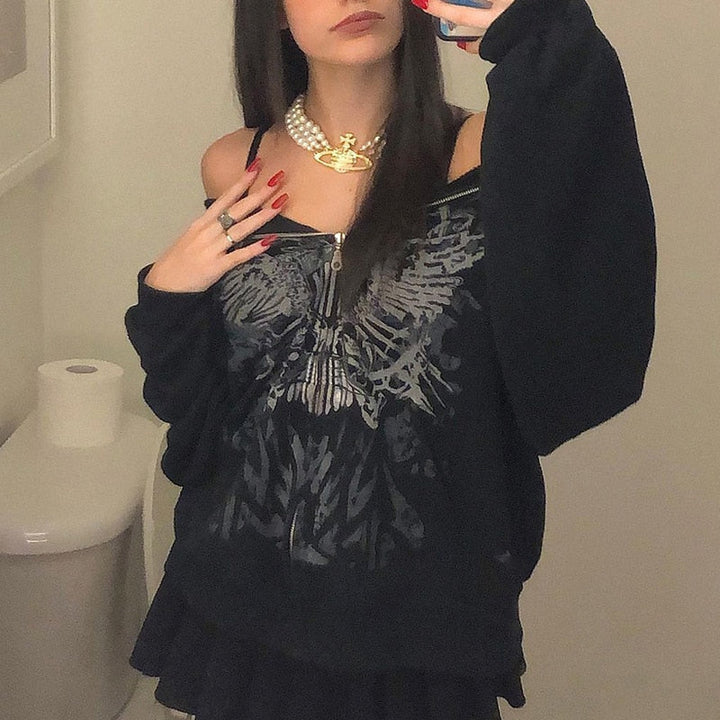 Frau in schwarzem Pullover mit Adler-Design, Perlenkette, schwarzer Rock, Badezimmer-Hintergrund.