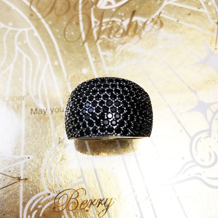 Schwarzer Damenring mit Strasssteinen, glänzend, elegantes Schmuckdesign auf goldenem Hintergrund.