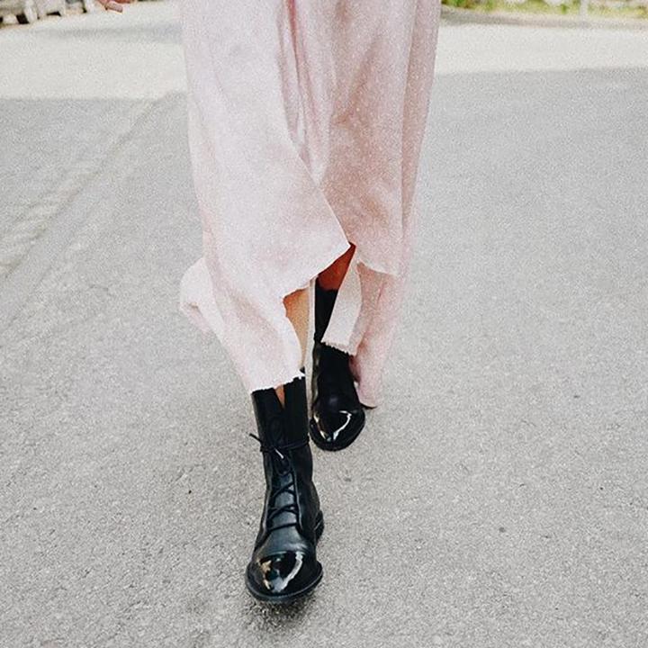 Frau in rosa Kleid mit schwarzen Lederstiefeln auf Asphaltweg.