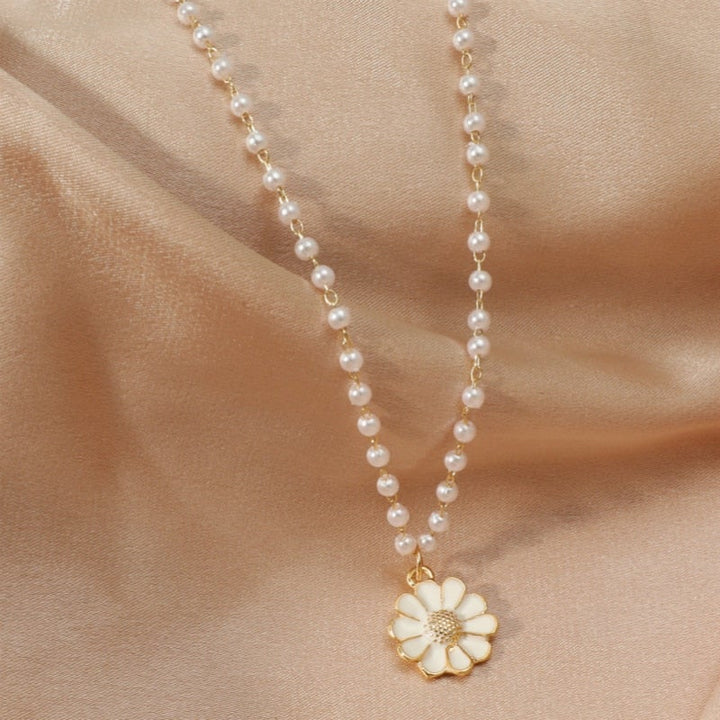 Perlenkette mit weißem Blumenanhänger auf beigem Stoff, eleganter Schmuck für Damen.