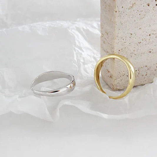 Zwei minimalistische Ringe, silber und gold, auf weißem Hintergrund neben Betonblock.