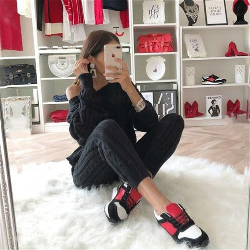 Frau in schwarzem Outfit mit rot-weißen Sneakers, sitzt auf weißem Teppich, modische Kleidung.