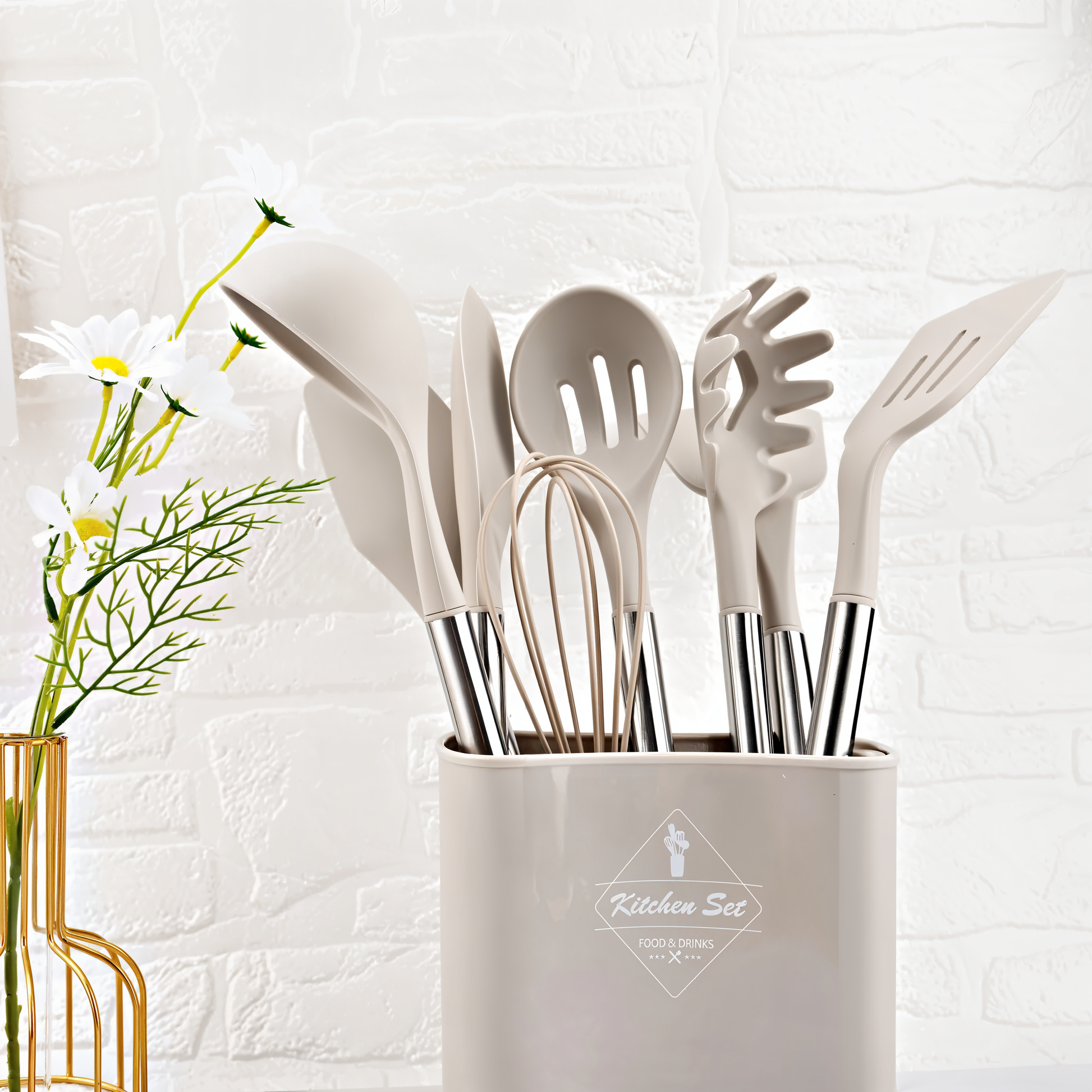 Beiges Küchenutensilien-Set aus Silikon und Edelstahl in Halter vor weißer Ziegelwand.