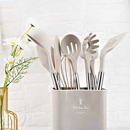 Beiges Küchenutensilien-Set aus Silikon und Edelstahl in Halter vor weißer Ziegelwand.