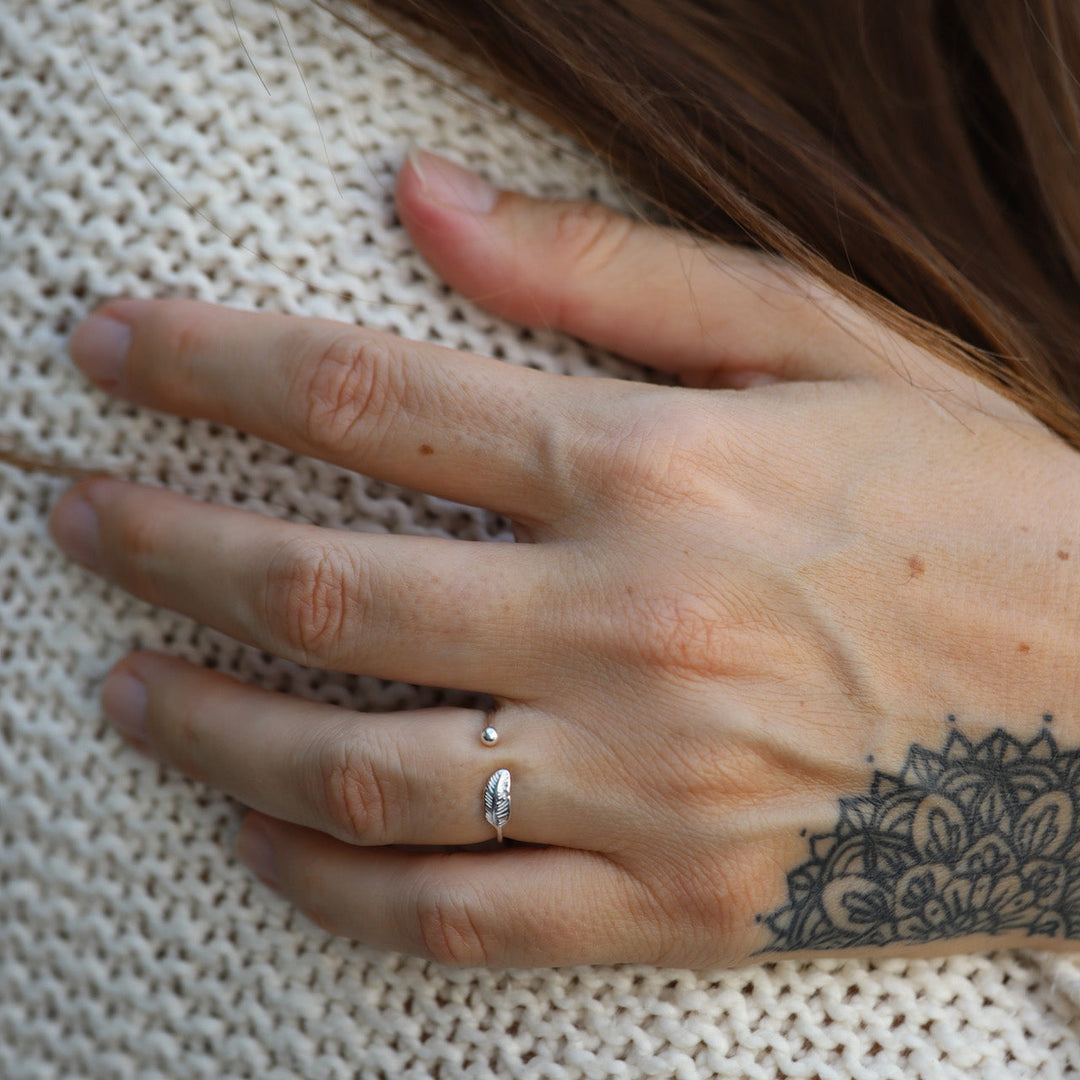 Silberner Verstellbarer Ring mit Blattdesign auf tätowierter Hand, gestrickter Hintergrund.