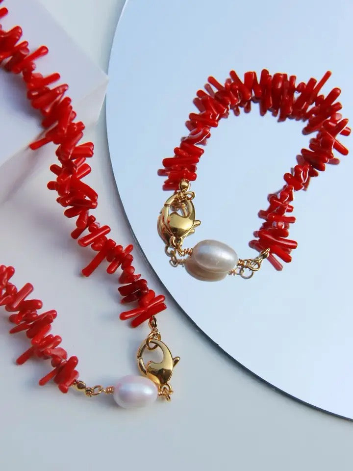 Rote Korallenarmbänder mit goldenen Verschlüssen und Perlen auf weißem Hintergrund.