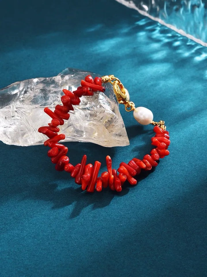 Rotes Korallenarmband mit goldener Schließe und Perle auf blauem Hintergrund.