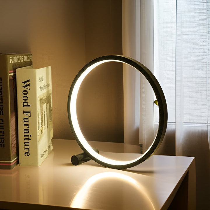 Moderne runde LED-Tischlampe auf weißem Tisch neben Büchern und Fenster im Wohnzimmer.