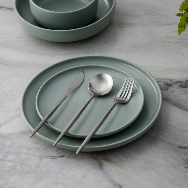Grünes Keramikgeschirr-Set mit Besteck auf Marmortisch, modern und stilvoll.