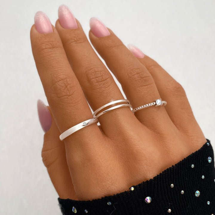 Drei silberne Ringe an Hand, einer mit Diamant, elegantes Schmuckdesign, Nahaufnahme.