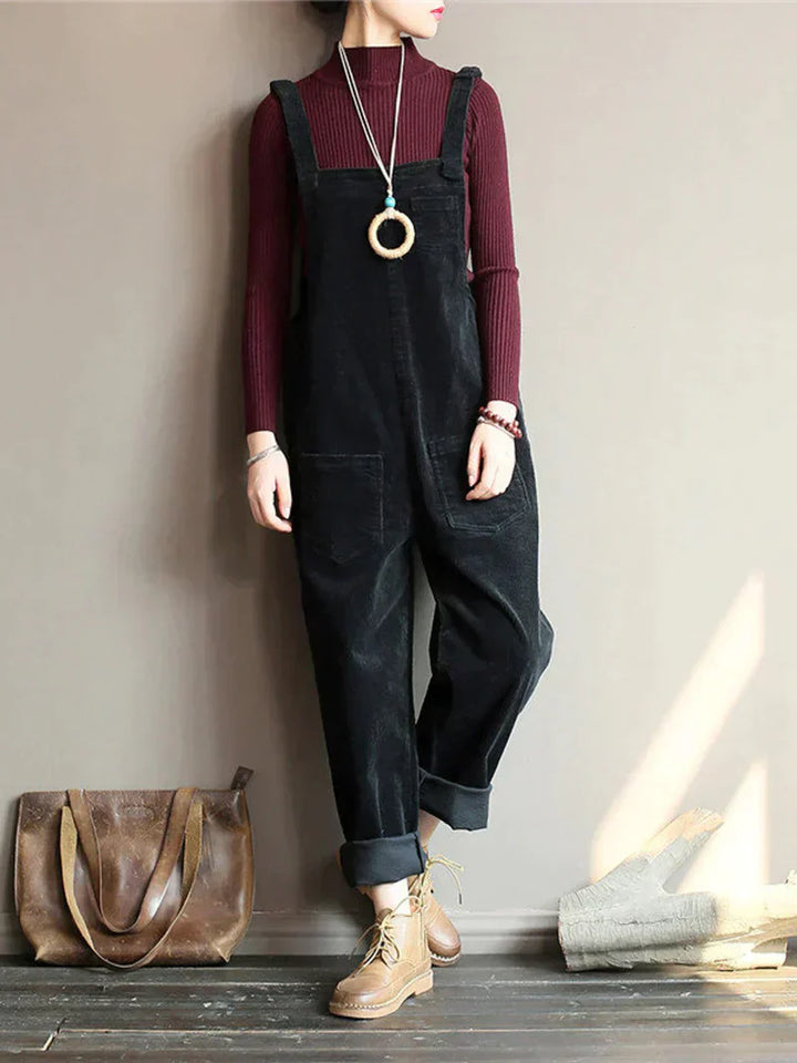 Frau in schwarzem Cord-Overall, rotem Pullover, braunen Stiefeln, braune Ledertasche.