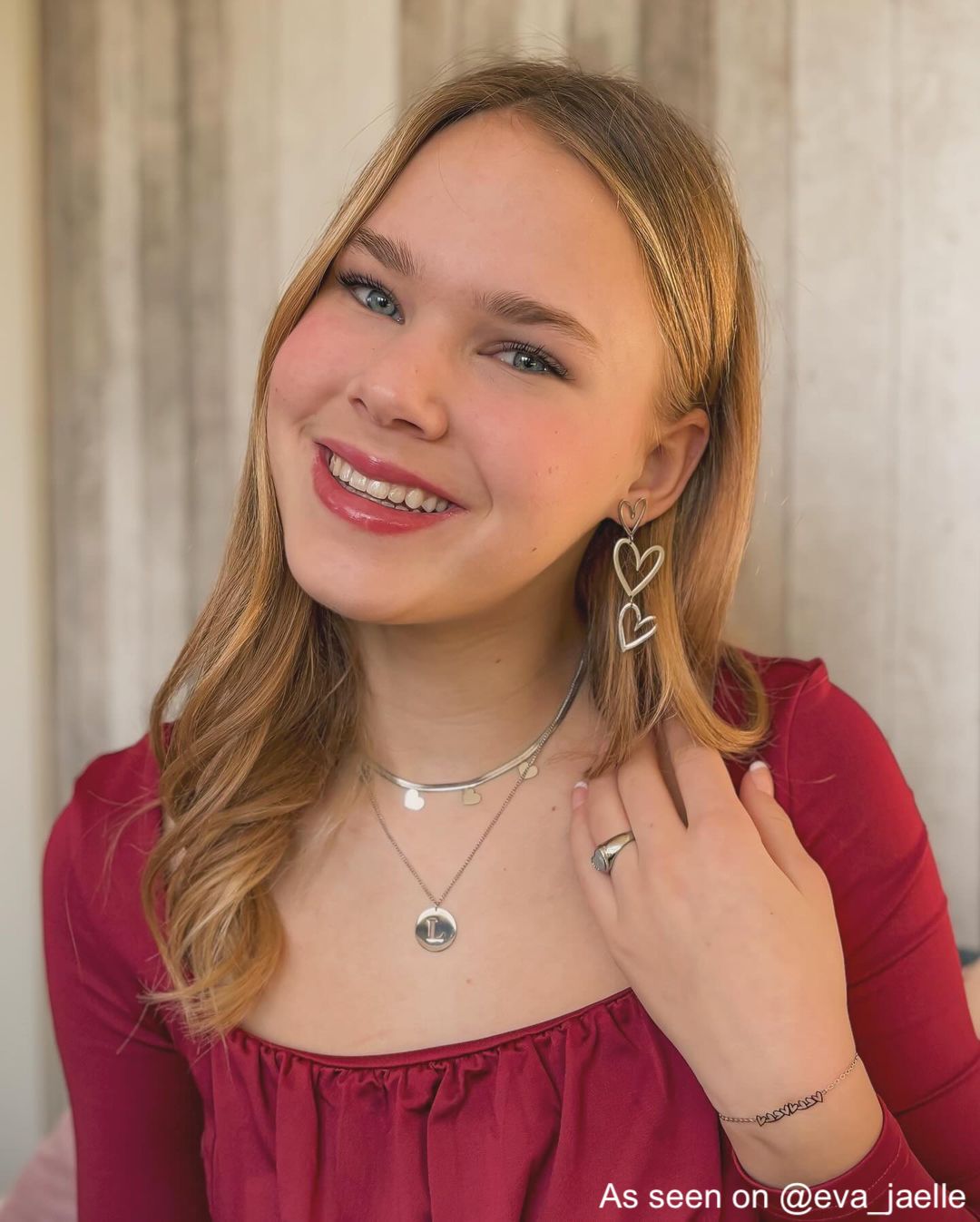 Frau trägt silberne Herz-Ohrringe, rotes Oberteil, lächelt, modisches Accessoire, Schmuck.