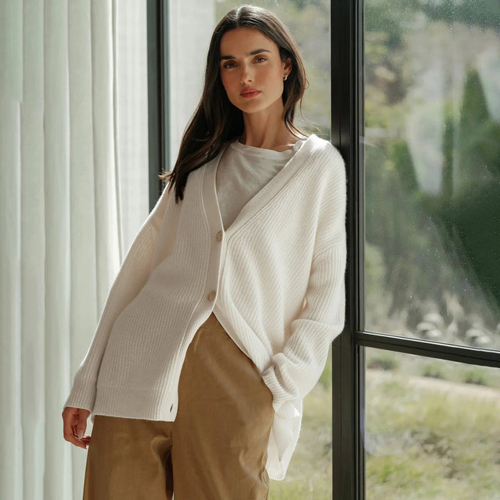 Frau trägt weißen Strick-Cardigan, lässig, modisch, vor Fenster stehend, Herbstmode.