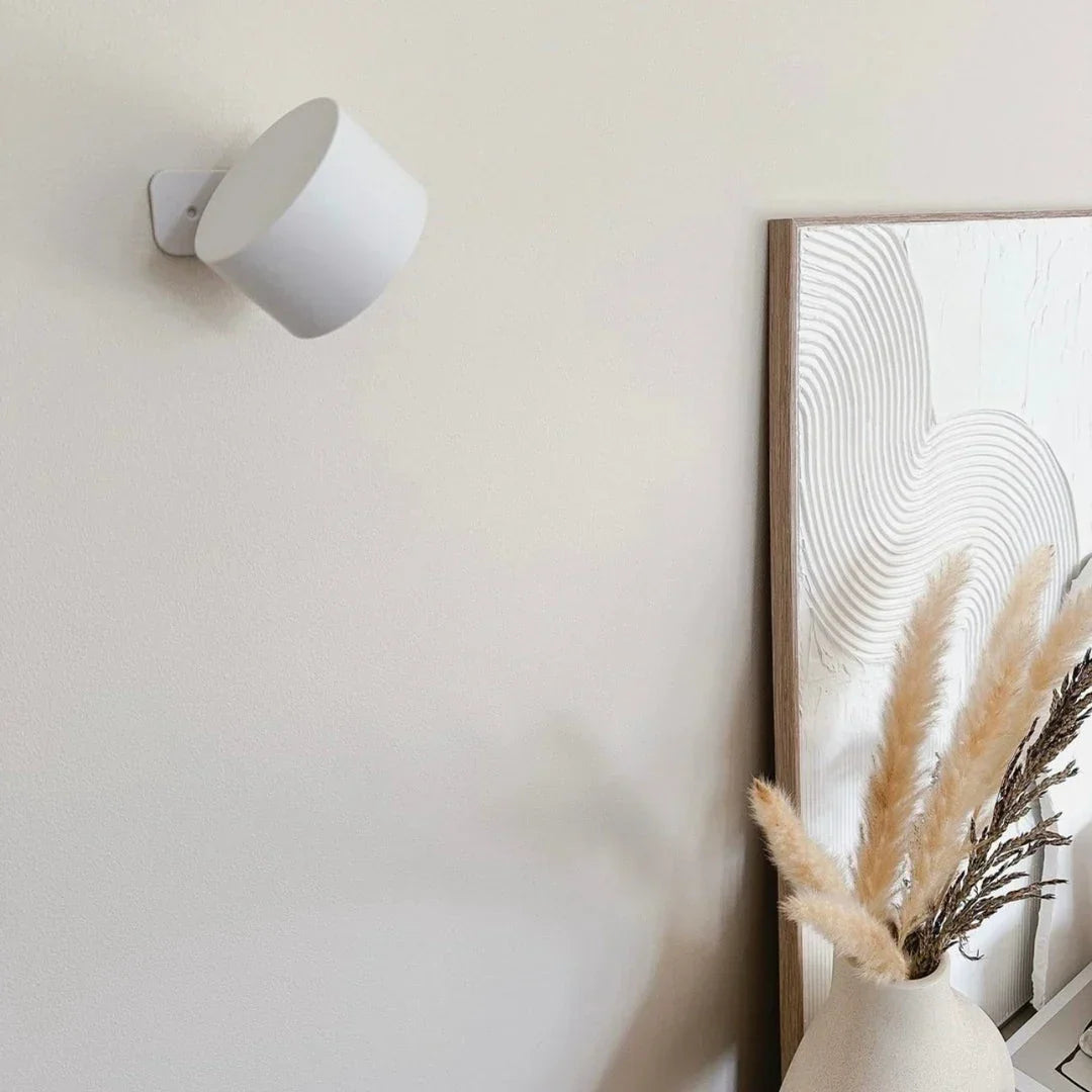 Vypnutá bílá lampa na světlé stěně vedle rámovaného obrazu a vázy s pampovou trávou 16