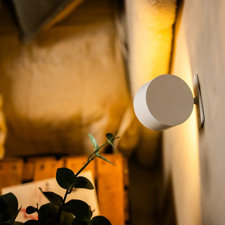 Bílá lampa zezadu s dotykovým ovládacím symbolem na zdi, v popředí rostlina 4