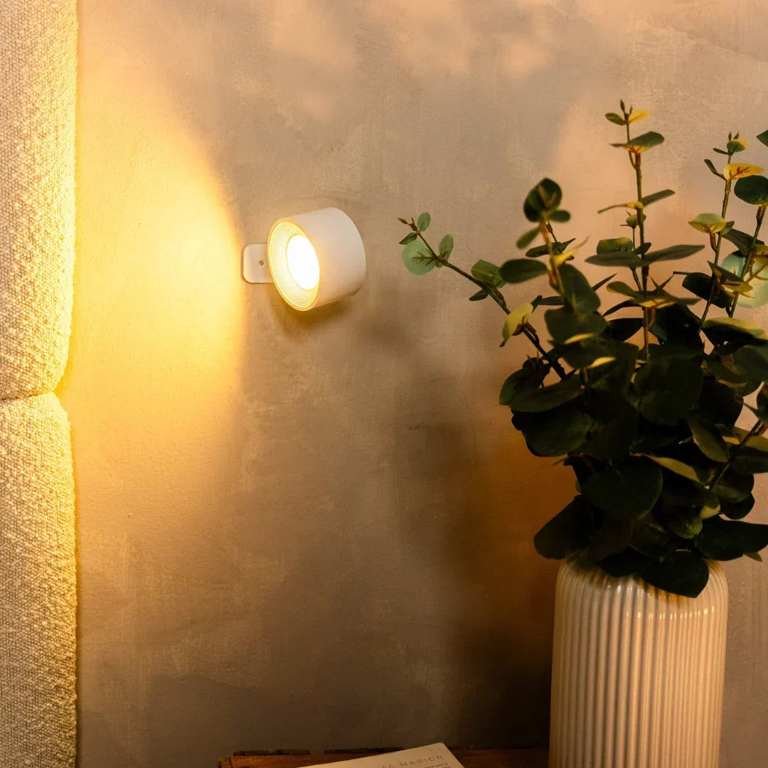 Bílá nástěnná lampa se zlatavým světlem vedle vázy s eukalyptem a čalouněného čela postele 6