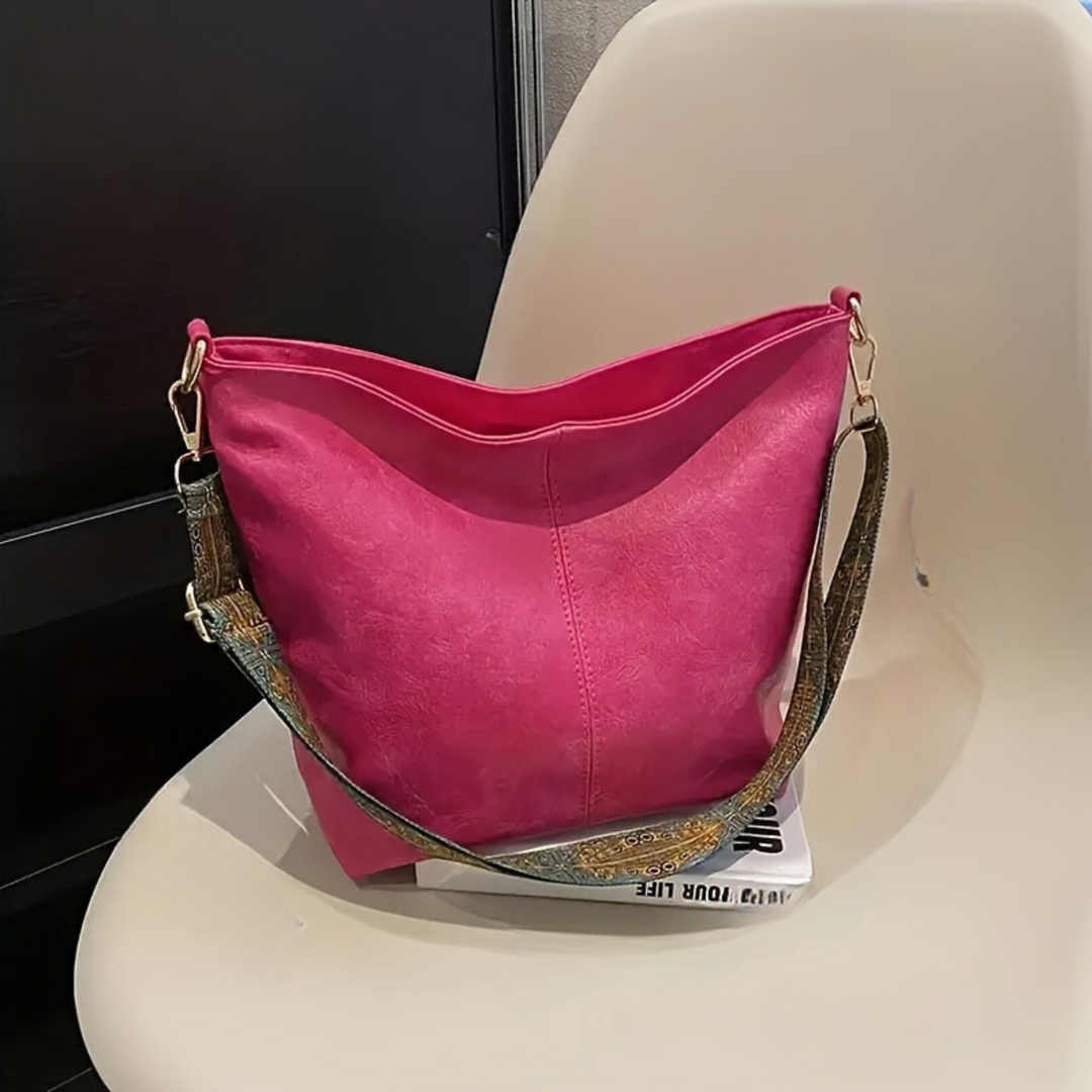 Rosa Damenhandtasche aus Leder mit verstellbarem Riemen auf einem Stuhl.