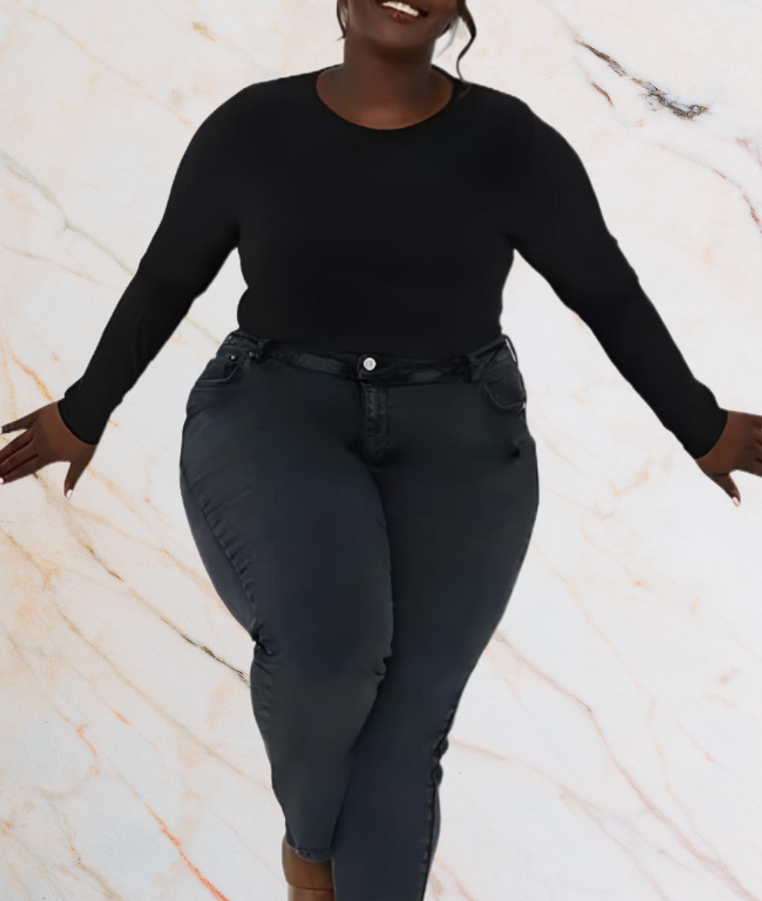 Frau in schwarzem Langarmshirt und Jeans vor marmoriertem Hintergrund.
