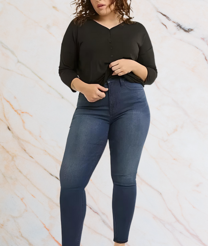 Frau in schwarzem Langarmshirt und blauer Jeans vor Marmorhintergrund.