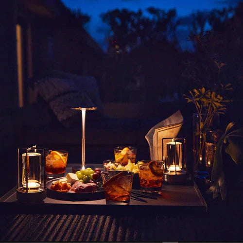 Abendliche Tischdekoration mit Kerzen, Getränken und Snacks im Freien bei Dämmerung.