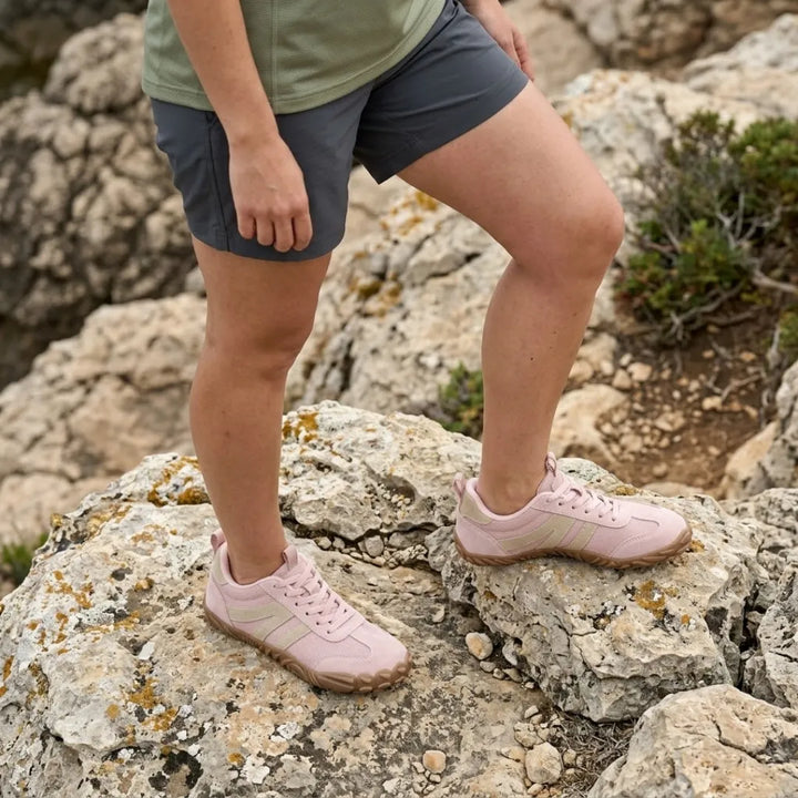 Žena v šortkách a zeleném tričku stojí na skalách v růžových barefoot teniskách s béžovými pruhy. 11