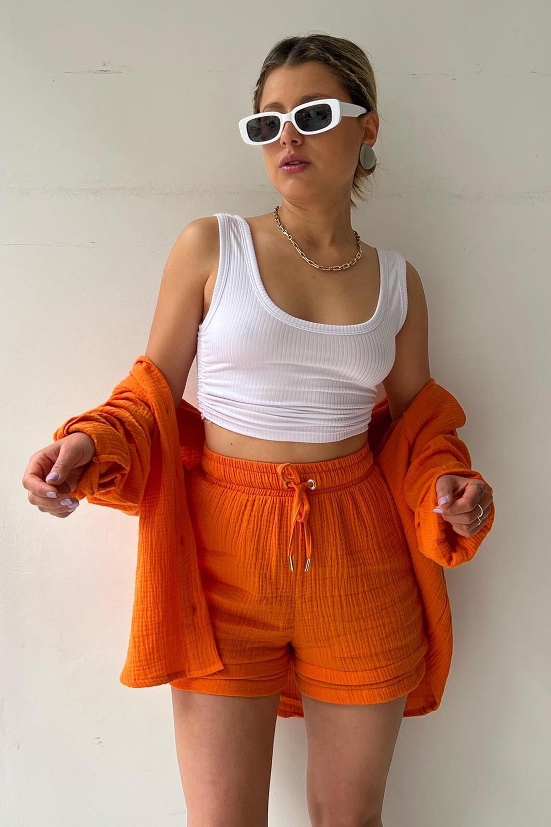 Frau in weißem Tanktop und orangefarbenem Shorts-Set, modisch, lässig, Sommerkleidung.