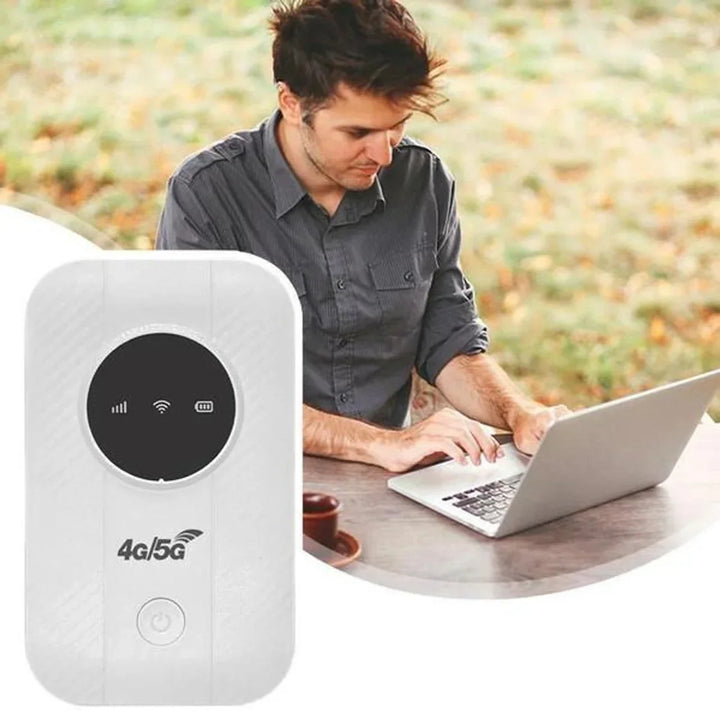 Bílý kapesní router s kulatým displejem, v pozadí muž pracující na notebooku u stolu venku 1