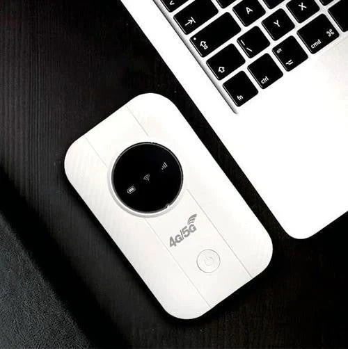 Pohled shora na bílý router položený na tmavém stole vedle klávesnice notebooku 5