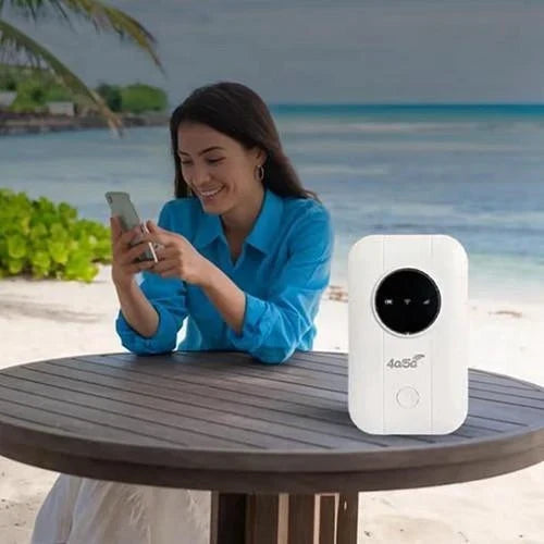 Usmívající se žena s telefonem u stolu na pláži, vedle ní stojí bílý router 6
