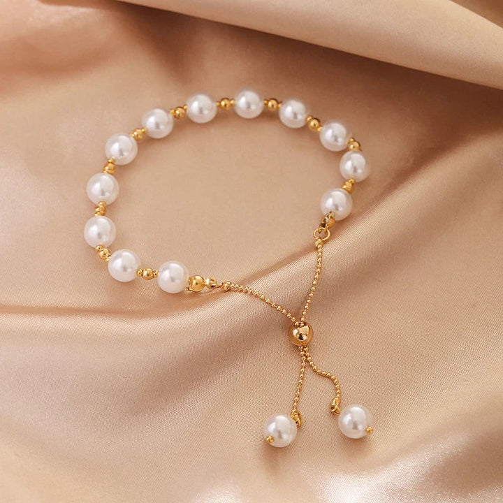 Goldenes Armband mit weißen Perlen auf beigem Stoff, eleganter Schmuck für Damen.
