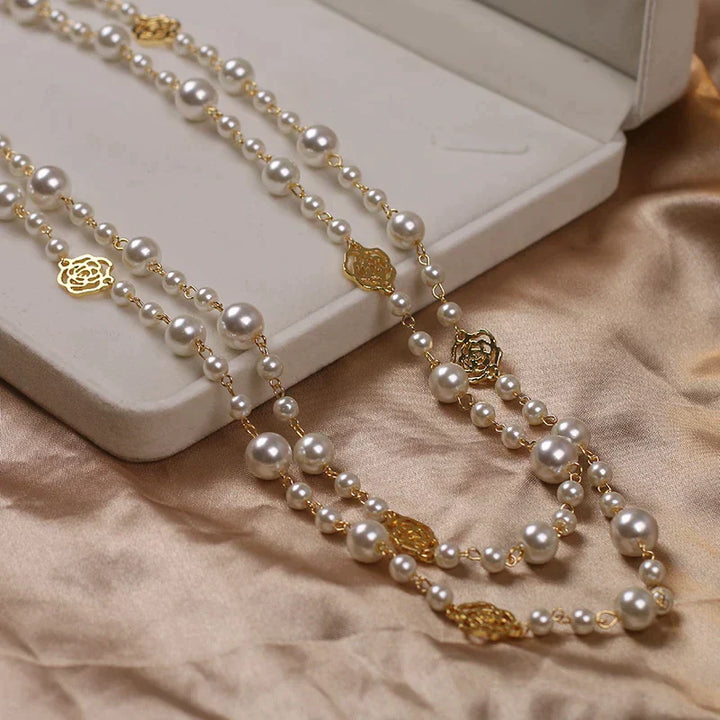 Lange Perlenkette mit goldenen Rosendetails auf beigem Stoff, eleganter Schmuck für Damen.