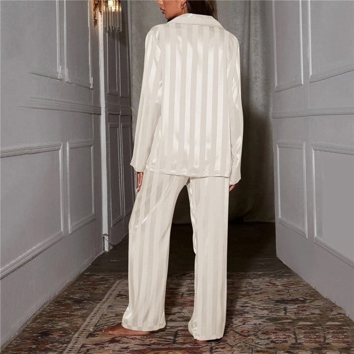 Frau in cremefarbenem Satin-Pyjama, gestreift, steht in elegantem Flur.